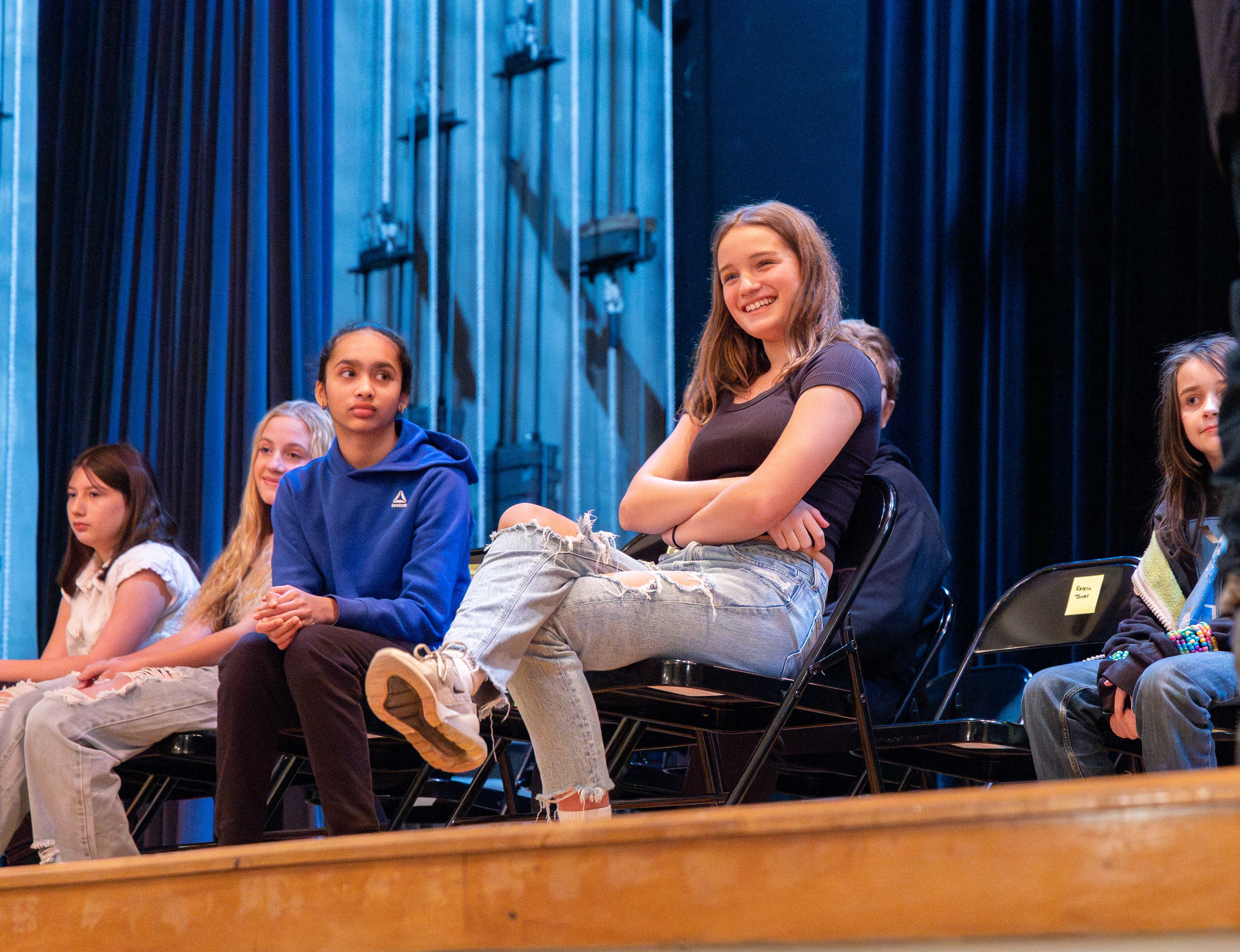 A student sitting on stage smiles to the crowd as she waits for her turn